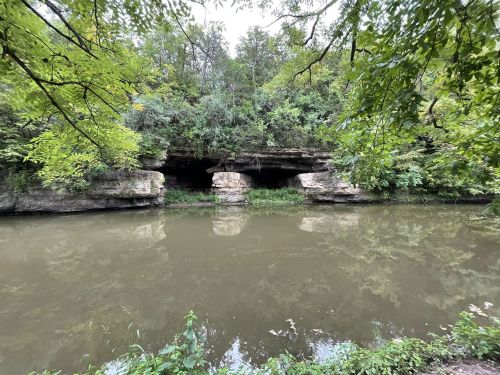 A serene river scene with rocky cliffs and lush greenery along the water's edge.