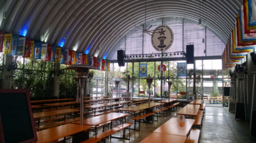 Interior of a spacious venue with long tables, colorful banners, and large windows, featuring a modern, industrial design.