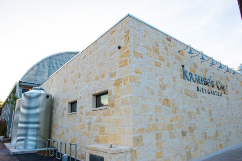 Exterior of Krause's Biergarten, featuring a stone wall and a large metal tank beside the building.