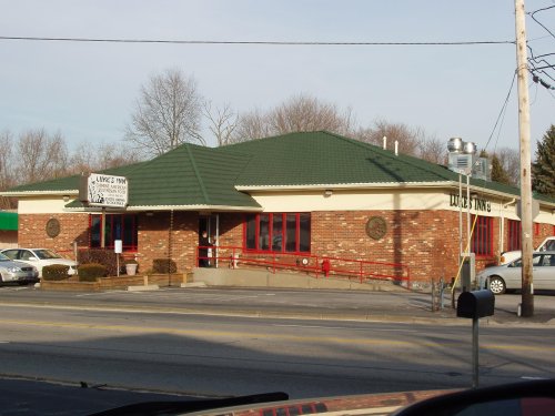 A brick building with a green roof, featuring large windows and a sign for "Lube's Inn," surrounded by parked cars.