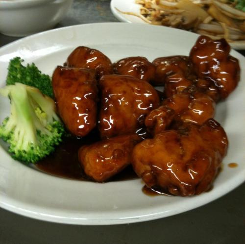 A plate of glazed chicken pieces with broccoli on the side, served in a dark sauce.