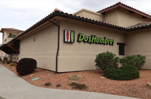 Exterior of a restaurant named "Dos Hombres," featuring a sign and landscaped area with shrubs and rocks.