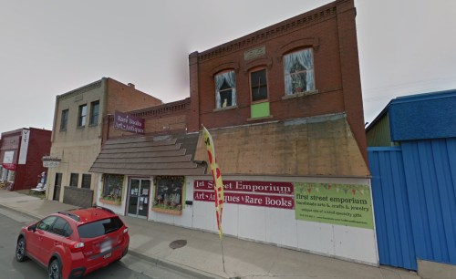 A red brick building with a sign for "1st Street Emporium" and a red car parked in front.