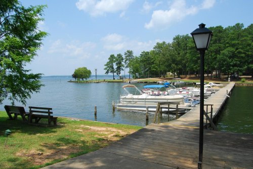 A serene lakeside view featuring a dock with boats, surrounded by trees and a clear blue sky.