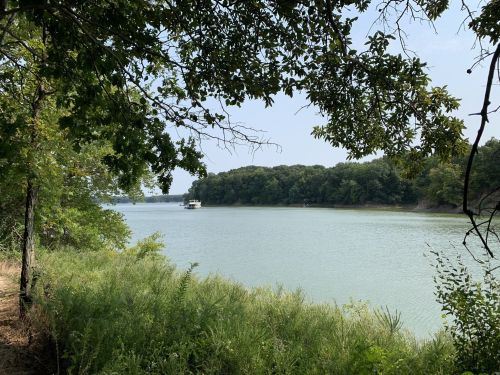 A serene river scene framed by trees, with a boat gently floating on the water in the distance.