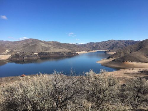 A serene landscape featuring a calm lake surrounded by mountains under a clear blue sky.