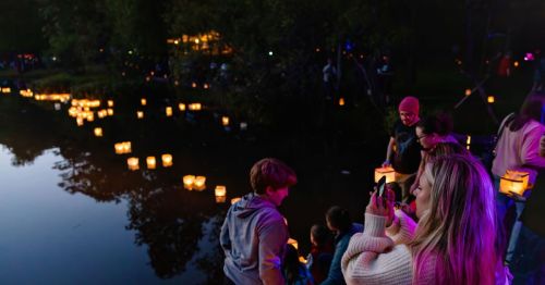 A serene scene by a river at dusk, with people releasing glowing lanterns into the water, creating a magical atmosphere.