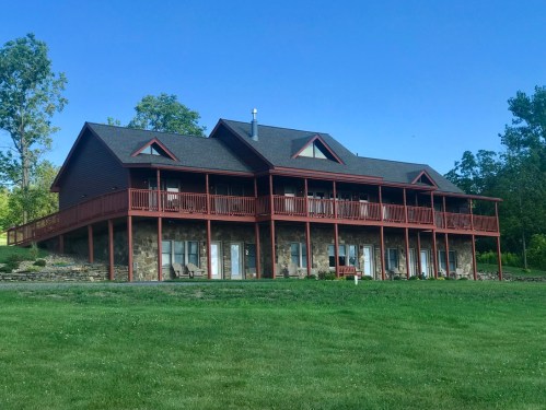 A large, two-story house with a red exterior and multiple balconies, surrounded by green grass and trees.