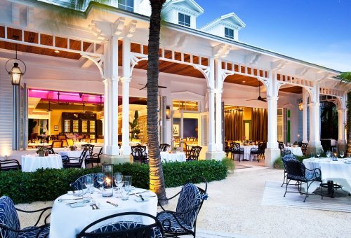 Elegant outdoor dining area with white architecture, palm trees, and tables set for dinner at twilight.