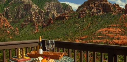 A scenic view of red rock mountains with a table set for two, featuring wine, glasses, and a cheese platter.