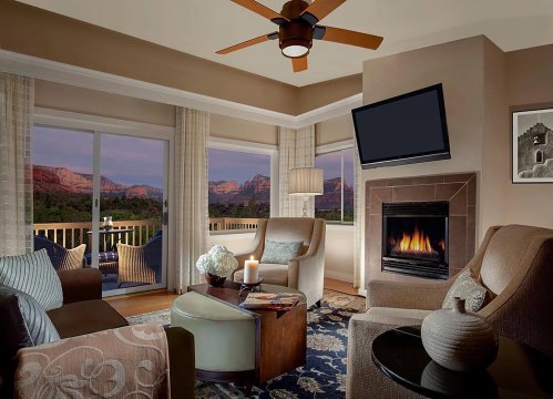 Cozy living room with a fireplace, modern furniture, and large windows showcasing a mountain view at sunset.