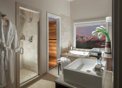 A modern bathroom featuring a shower, bathtub, and a scenic window view of mountains at sunset.