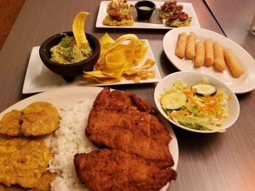A spread of delicious food including fried fish, rice, tostones, guacamole, salad, and appetizers on a table.