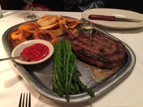A plated meal featuring a ribeye steak, asparagus, onion rings, and a side of ketchup on a silver tray.