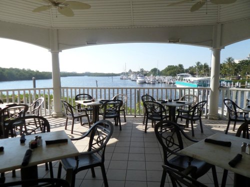 View from a restaurant patio overlooking a calm waterway with boats and lush greenery in the background.