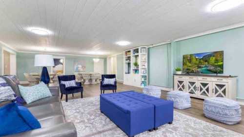 A modern living room with a gray sofa, blue ottoman, and a TV, featuring light walls and decorative accents.