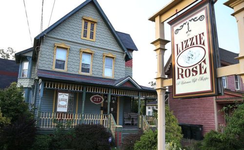 A colorful Victorian house with a sign reading "Lizzie Rose" in front, featuring a porch and decorative details.