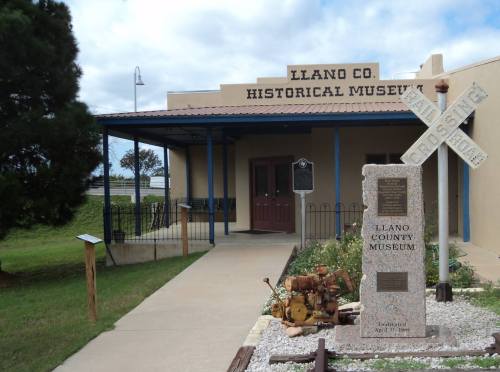 Exterior of the Llano County Historical Museum, featuring a stone monument and railroad crossing sign.