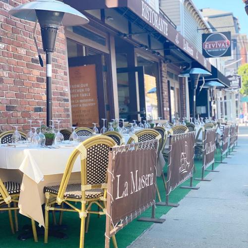 Outdoor dining setup at a restaurant with tables, chairs, and banners, featuring a cozy atmosphere.