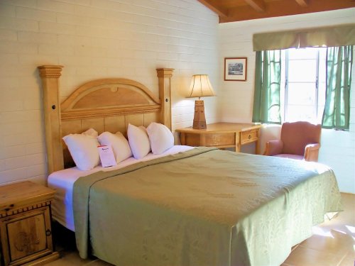 Cozy bedroom with a wooden bed, green bedspread, bedside table, lamp, and a chair by a window with green curtains.