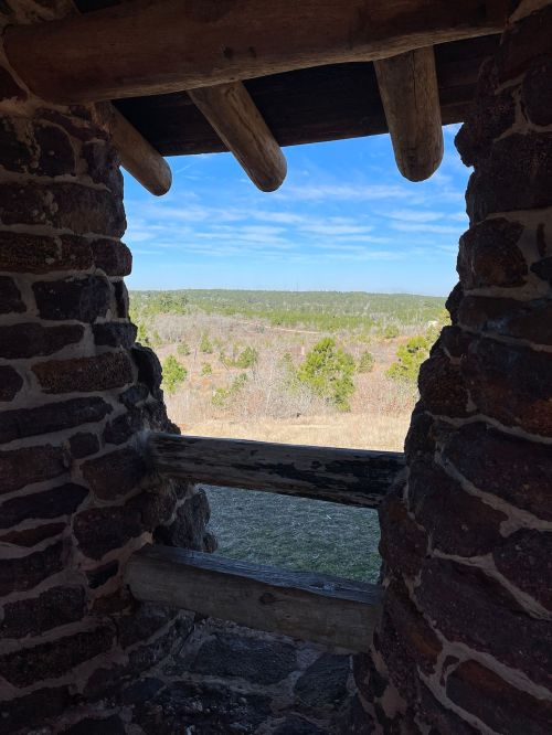 View from a stone structure, showcasing a landscape of trees and blue sky in the distance.