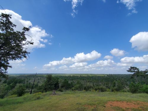 A panoramic view of a lush green landscape under a bright blue sky with fluffy white clouds.