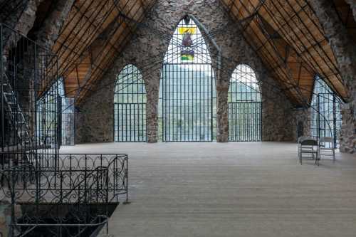 Interior of a stone building with a high wooden ceiling, large arched windows, and a simple wooden floor.