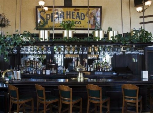 A vintage bar with a wooden counter, glassware, and lush greenery, featuring an old Spear Head sign on the wall.