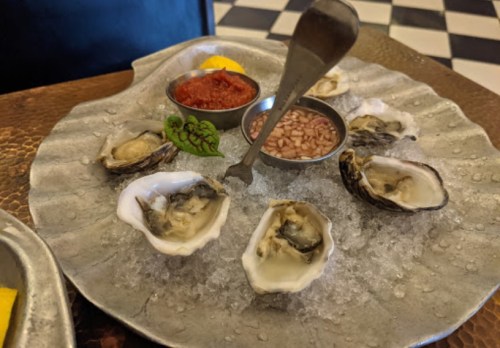A platter of fresh oysters on ice, accompanied by sauces and garnishes, served on a decorative metal dish.