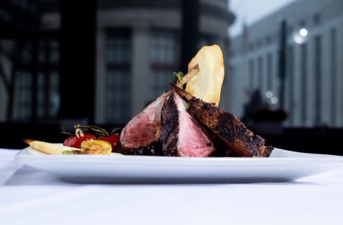 A beautifully plated dish featuring sliced meat, garnished with vegetables and a decorative slice of pear.