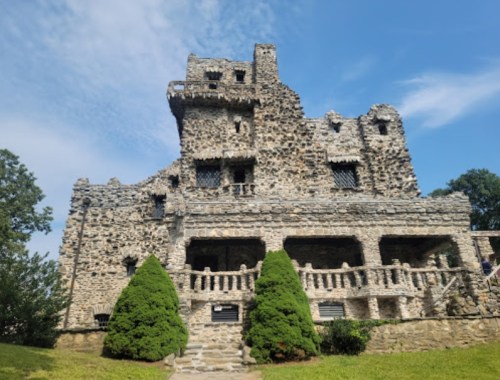 A stone castle with multiple levels and turrets, surrounded by greenery under a blue sky.