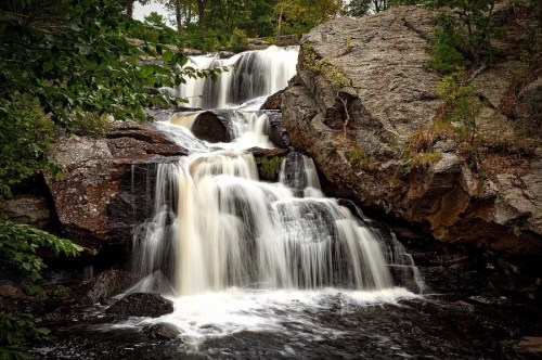 A serene waterfall cascading over rocky terrain, surrounded by lush greenery and trees.