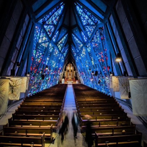 Interior of a modern church with vibrant stained glass windows and empty wooden pews, creating a serene atmosphere.