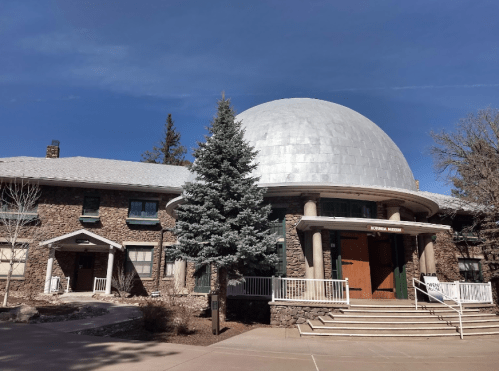 A stone building with a large dome, surrounded by trees and a clear blue sky.