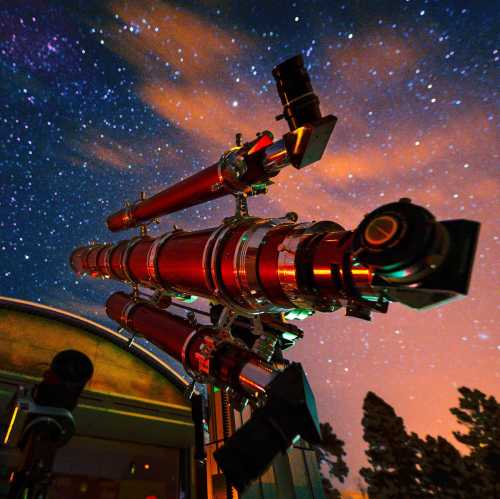 A telescope points towards a starry night sky, with vibrant colors and clouds in the background.