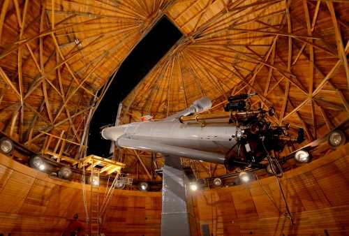 A large telescope inside a wooden observatory with a domed ceiling, showcasing intricate architectural details.