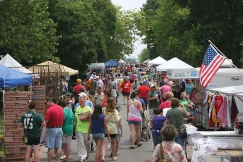 A bustling outdoor market with crowds of people, tents, and food stalls under a clear sky.