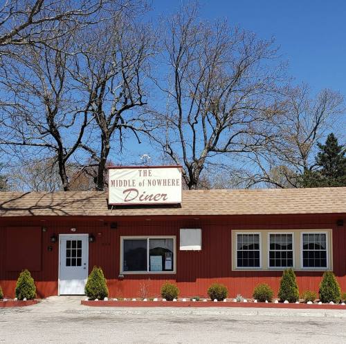 A red diner with a sign reading "The Middle of Nowhere Diner," surrounded by trees and a clear blue sky.