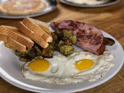 A plate of breakfast featuring two fried eggs, ham, golden-brown potatoes, and slices of toasted bread.