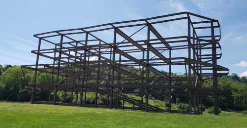 A large, skeletal steel structure stands in a green field under a clear blue sky.