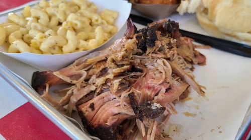A plate featuring pulled pork, macaroni and cheese, and a bun, served on a metal tray.