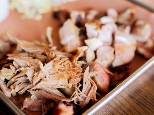 A close-up of shredded and chopped cooked meat on a tray, showcasing tender, juicy pieces.