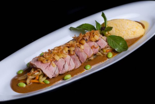 A beautifully plated dish featuring sliced pork tenderloin topped with crispy onions, served with polenta and sauce.