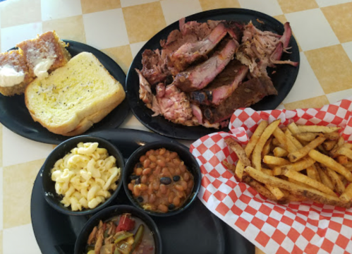 A plate of barbecue ribs, pulled pork, garlic bread, macaroni and cheese, baked beans, and French fries.