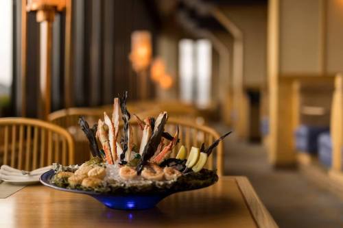 A beautifully arranged seafood platter with shrimp, oysters, and garnishes, set on a wooden table in a restaurant.