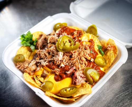 A takeout container filled with nachos topped with cheese, pulled pork, jalapeños, and salsa.