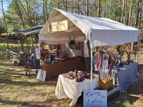 A tent displaying handmade leather goods and crafts, set in a wooded outdoor area.