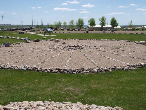 A circular stone arrangement in a grassy area, with a clear blue sky and distant trees in the background.