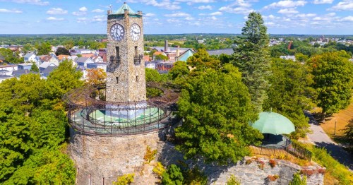 Aerial view of a historic stone clock tower at Jenks Park in RI, surrounded by greenery, overlooking the town of Central Falls, RI.