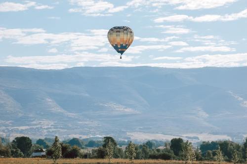 A colorful hot air balloon floats above a scenic landscape with mountains and trees under a blue sky.